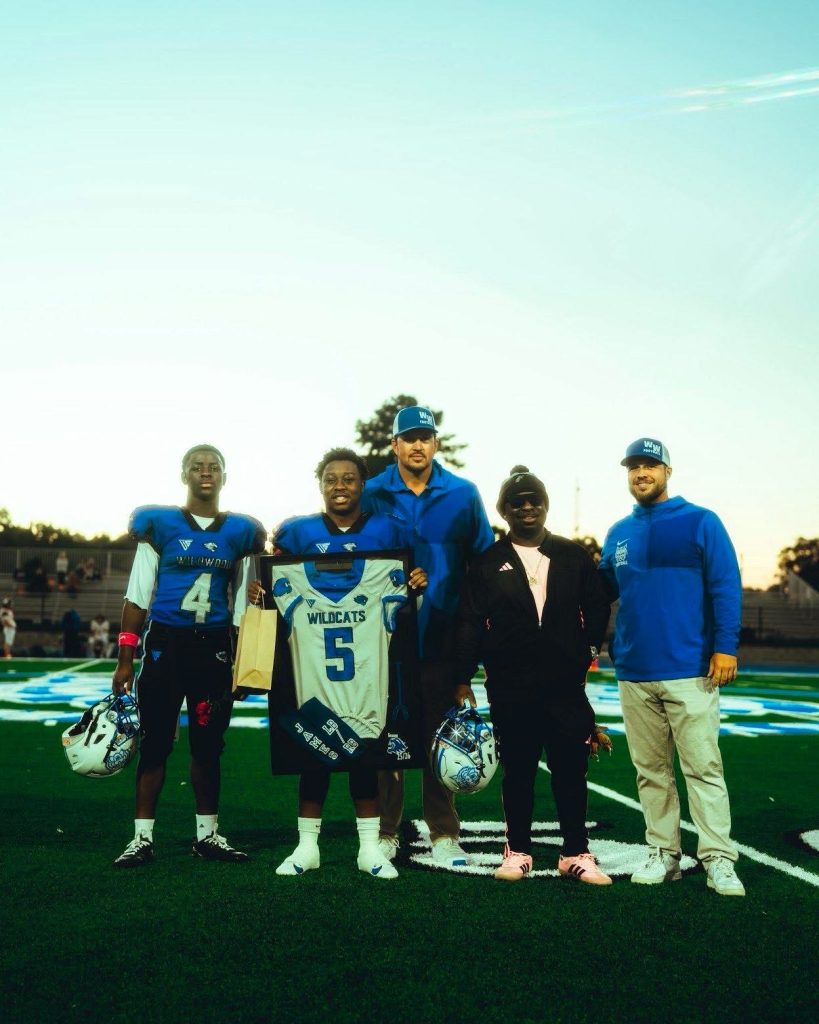 Wildwood Wildcats players and coaches standing together on the field at dusk.