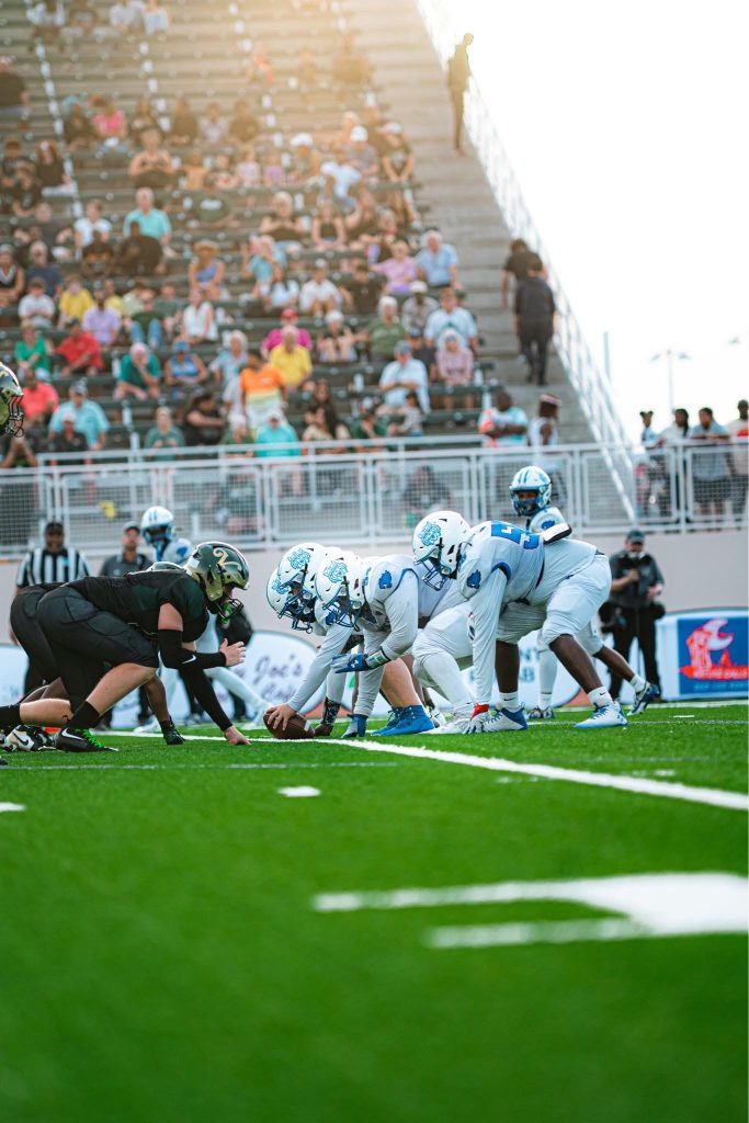 Wildwood Wildcats players at the line of scrimmage in front of a full grandstand.