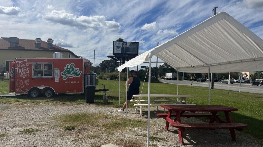 The Taqueria La Famosa truck with a white canopy over red picnic tables.