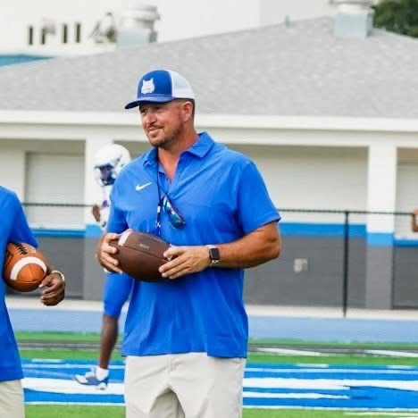 Coach Rhett Caruthers holding a football on the Wildwood practice field.